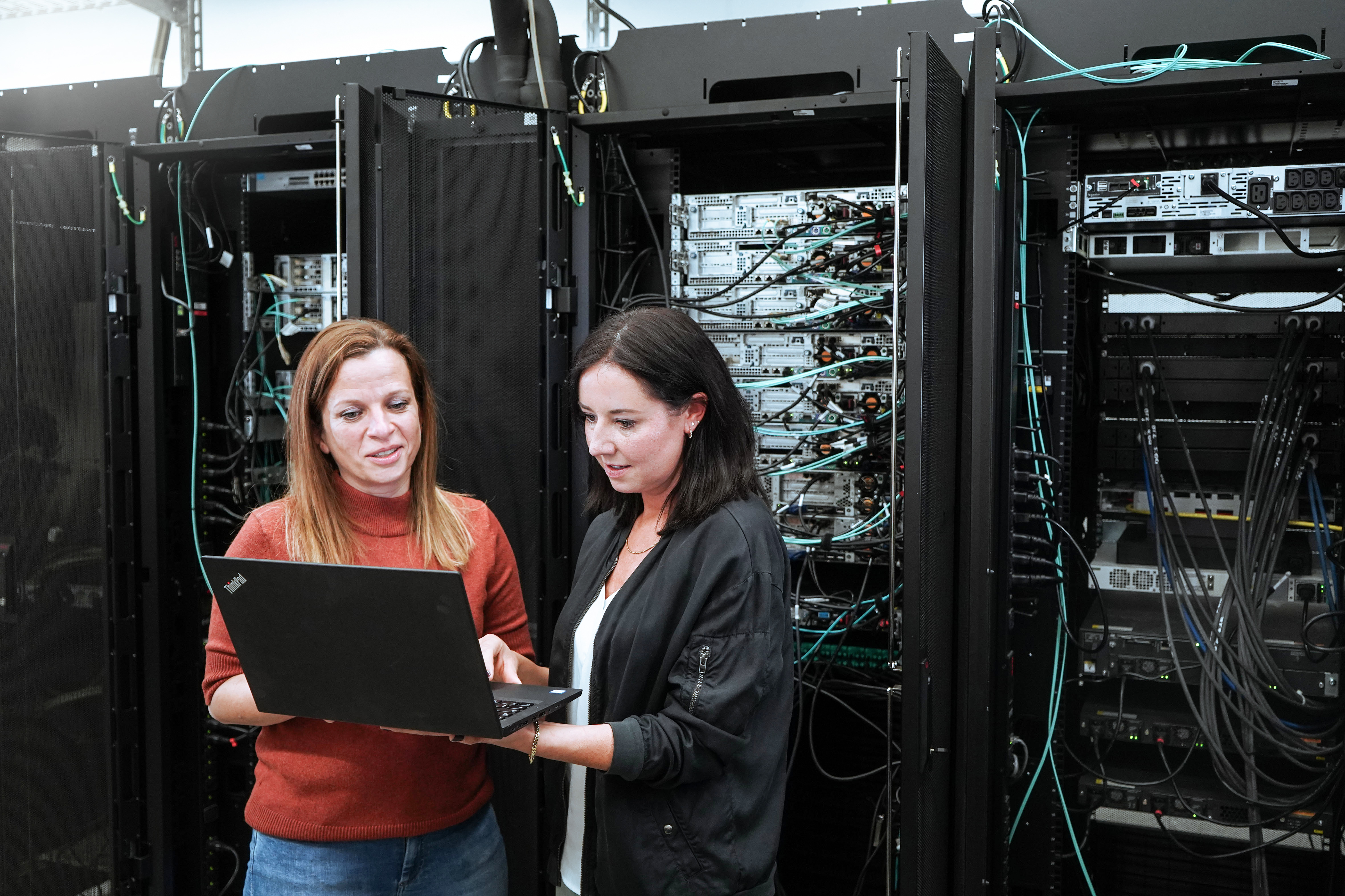 Zwei MVB Mitarbeiterinnen mit einem Laptop vor einem Netzwerk-Serverraum