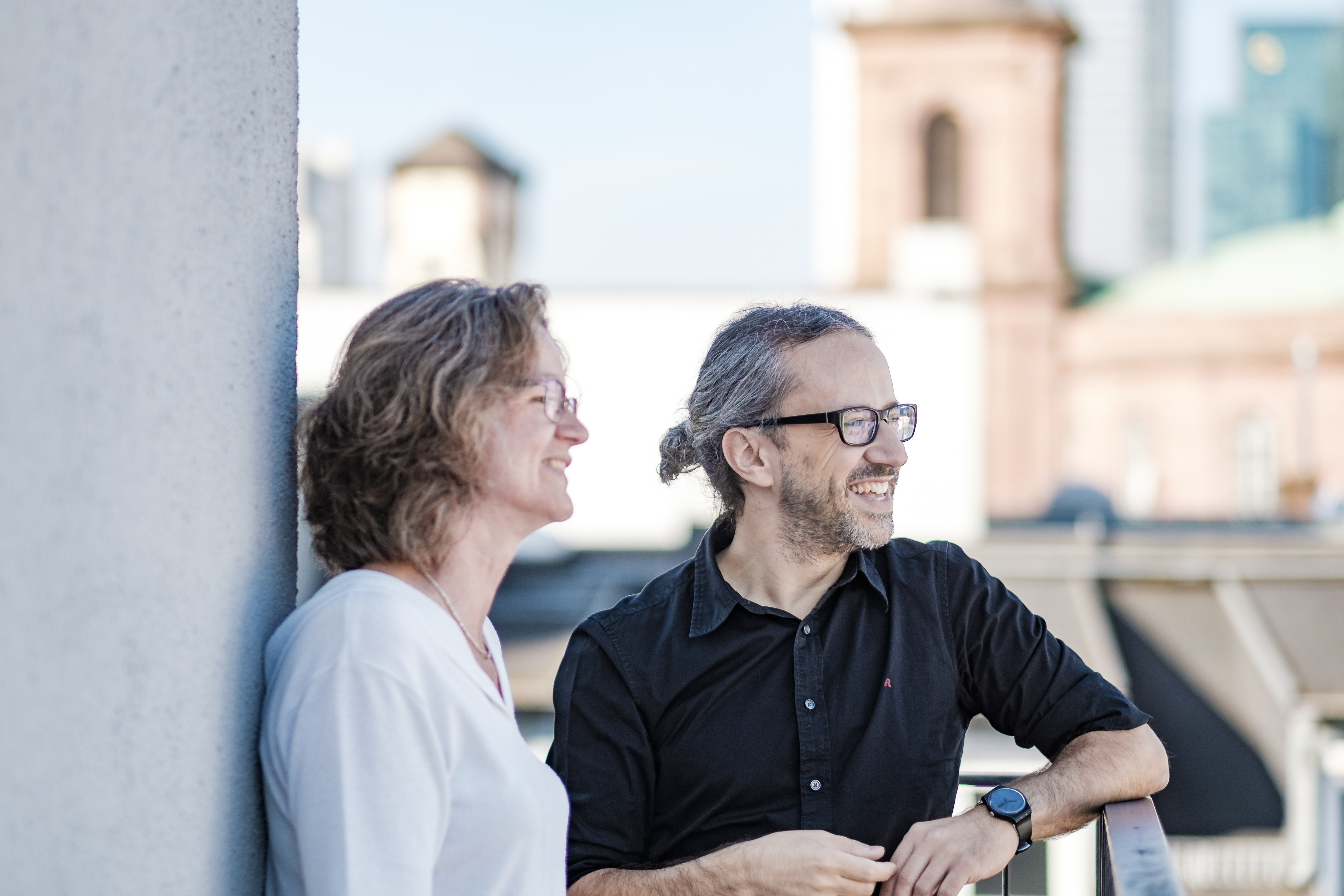 Eine Frau und ein Mann stehen auf einem Balkon und schauen auf die Frankfurter Innenstadt