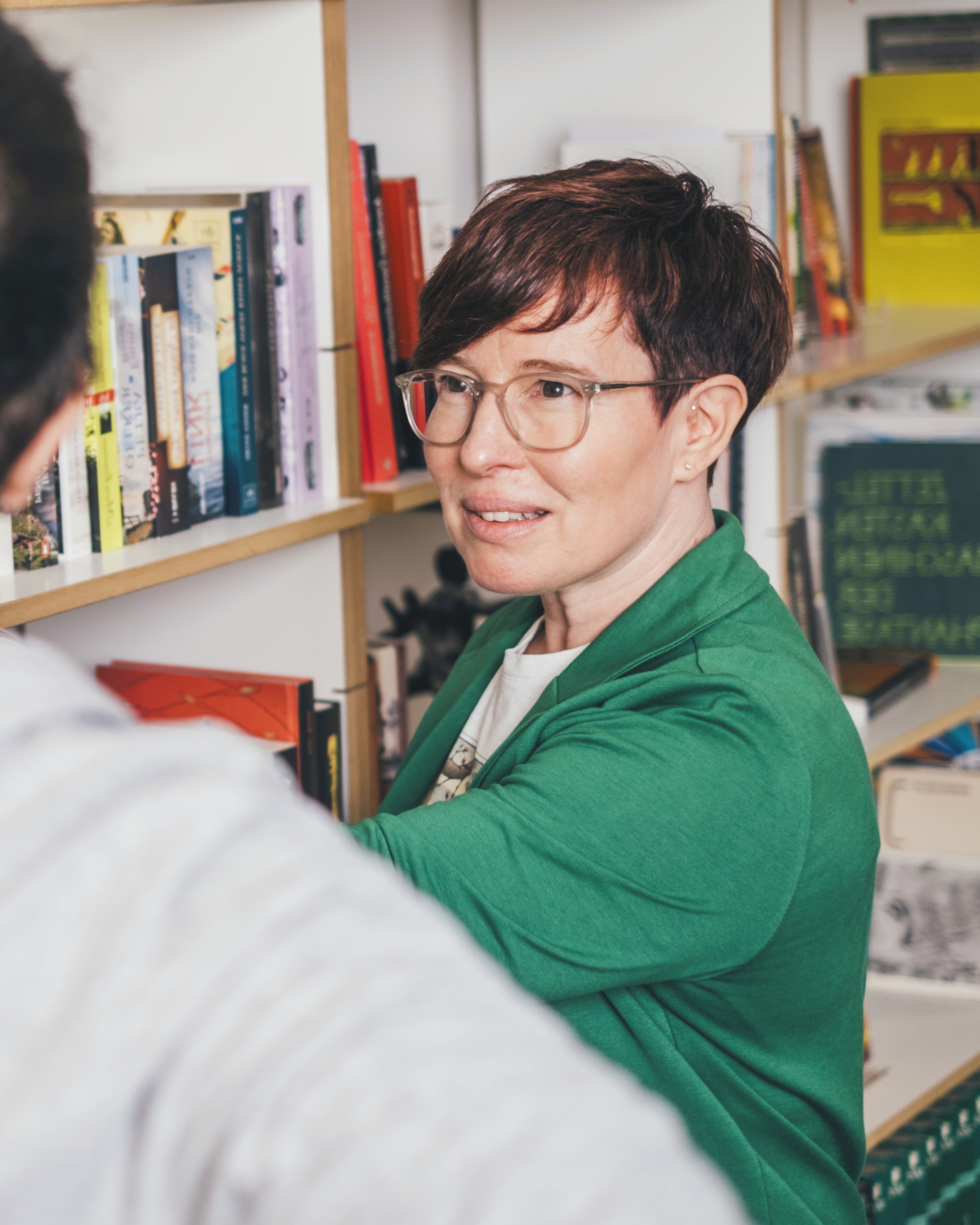 Silke steht vor einem Bücherregal und erklärt einer Person etwas