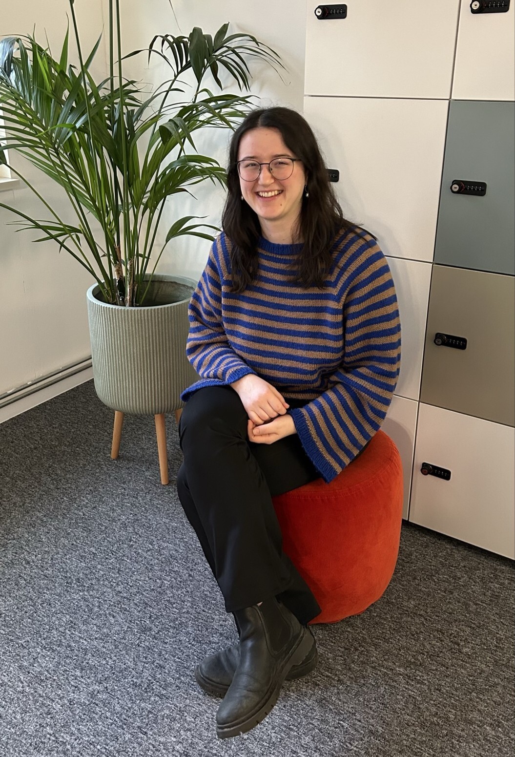 Franziska sitzt auf einem roten Hocker neben einer Pflanze