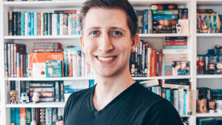 Ein Mann steht vor einem Bücherregal und lächelt.
