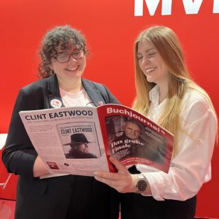 Vanessa und Olivia stehen vor einer roten Wand und schauen zusammen in das Buchjournal Magazin