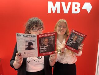 Vanessa und Olivia stehen nebeneinander vor einer roten Wand und schauen jeweils in ein Buchjournal Magazin.