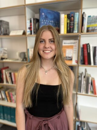 Olivia Zielke steht vor einem Bücherregal und lächelt.
