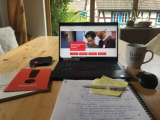 Ein Schreibtisch auf dem Schreibunterlagen, ein Laptop und eine Tasse stehen.