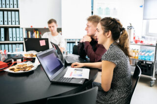 Eine Frau und zwei Männer sitzen mit jeweils einem Laptop an einem Tisch.