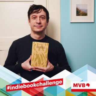 Anjo Schwarz hält im Rahmen der Indiebookchallenge im Dezember das Buch "Die Vögel" in den Händen und lächelt.