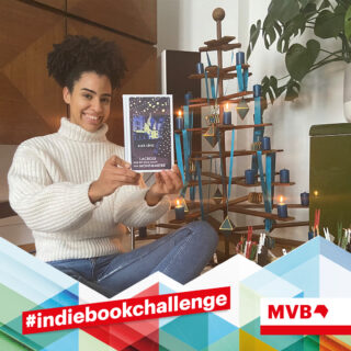 Taina de Miranda Soares hält im Rahmen der Indiebookchallenge im Dezember das Buch "Lacroix und die Stille Nacht von Montmartre" in den Händen und Lächelt.