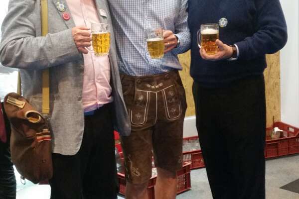 Drei Männer stehen nebeneinander, halten jeweils ein Glas mit Bier in der Hand und lächeln.