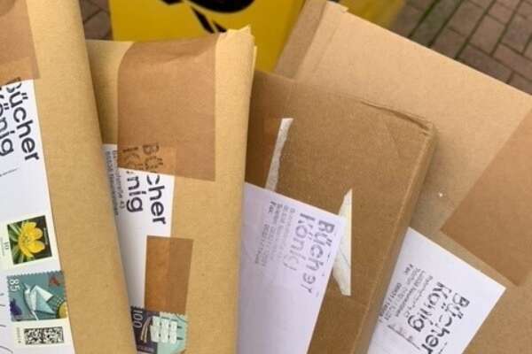 Vier Versandtaschen sind aufgefächert vor einem Briefkasten.