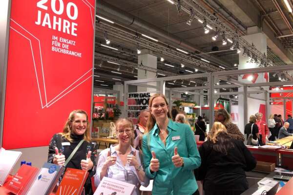 Drei Frauen stehen hinter der Infotheke und zeigen Daumen nach oben