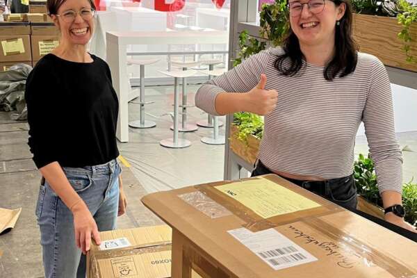 Berit Smolla und Franziska Werum stehen bei verpackten Kisten und lächeln in die Kamera