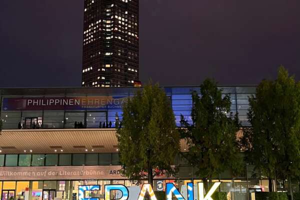 Frankfurt-Schild bei Nacht mit dem beleuchteten Messeturm im Hintergrund