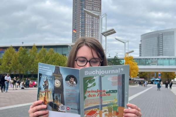 Miriam Schumm liest das Buchjournal, im Hintergrund sieht man den Messeturm