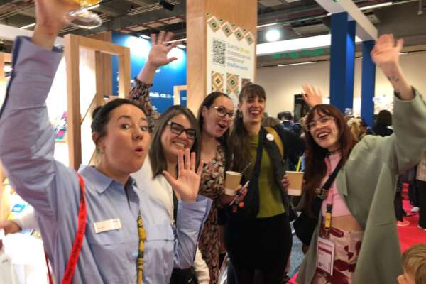 Ines, Carina, Katrin, Rahel und Lorina stehen zusammen, schauen in die Kamera und heben die Arme