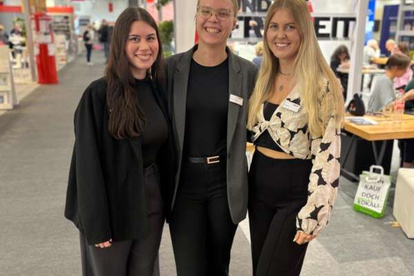 Yelda, Ronja und Olivia stehen Arm in Arm und lächeln in die Kamera