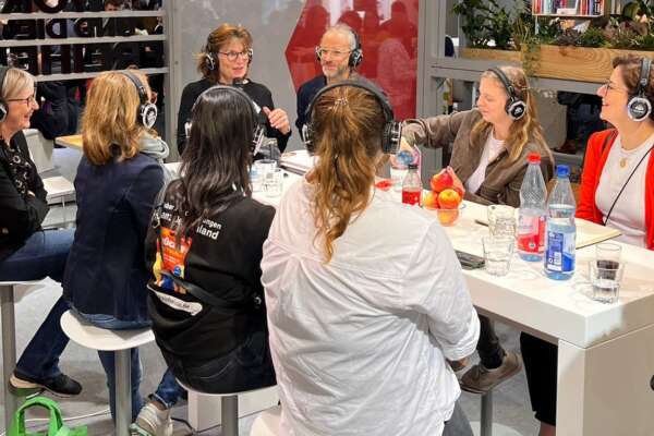 Die Teilnehmer des MVB-Austauschs sitzen zusammen am Tisch und tragen Kopfhörer.