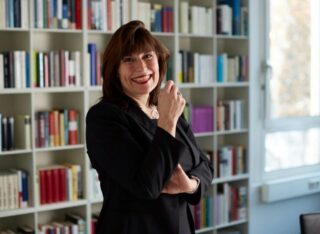 Stephanie Lange steht vor einem Bücherregal und lächelt.