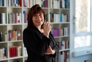Stephanie Lange steht vor einem Bücherregal und lächelt.