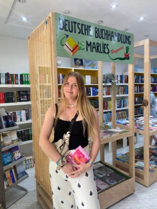 Olivia steht vor einem Bücherregal, hält ein Buch in den Händen und lächelt.