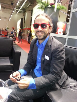 Markus sitzt auf einem schwarzen Sofa, trägt eine Sonnenbrille und lächelt.