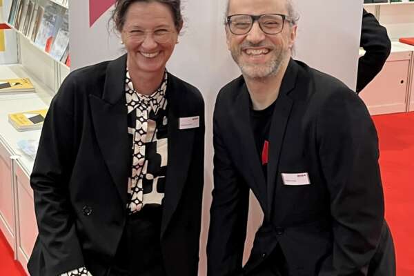 Eine Frau und ein Mann am Stand von Livro auf der LBM vor einer Fotowand.