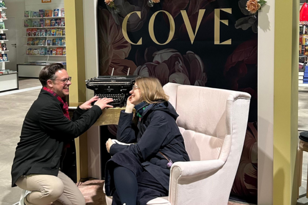 Thomas tippt in eine Schreibmaschine und Angie sitzt auf einem Ohrensessel an einem Foto-Spot.