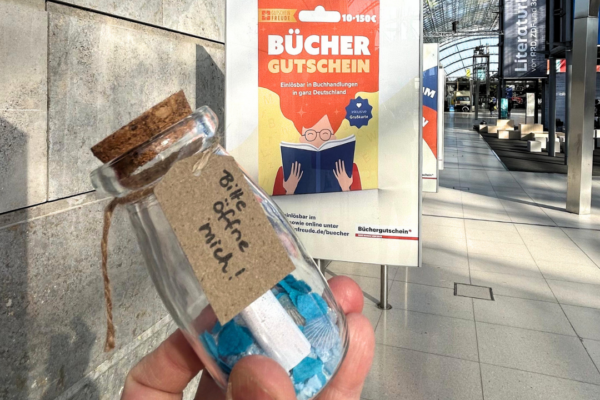 Eine Flaschenpost wird vor das Büchergutschein-Plakat auf der LBM gehalten.